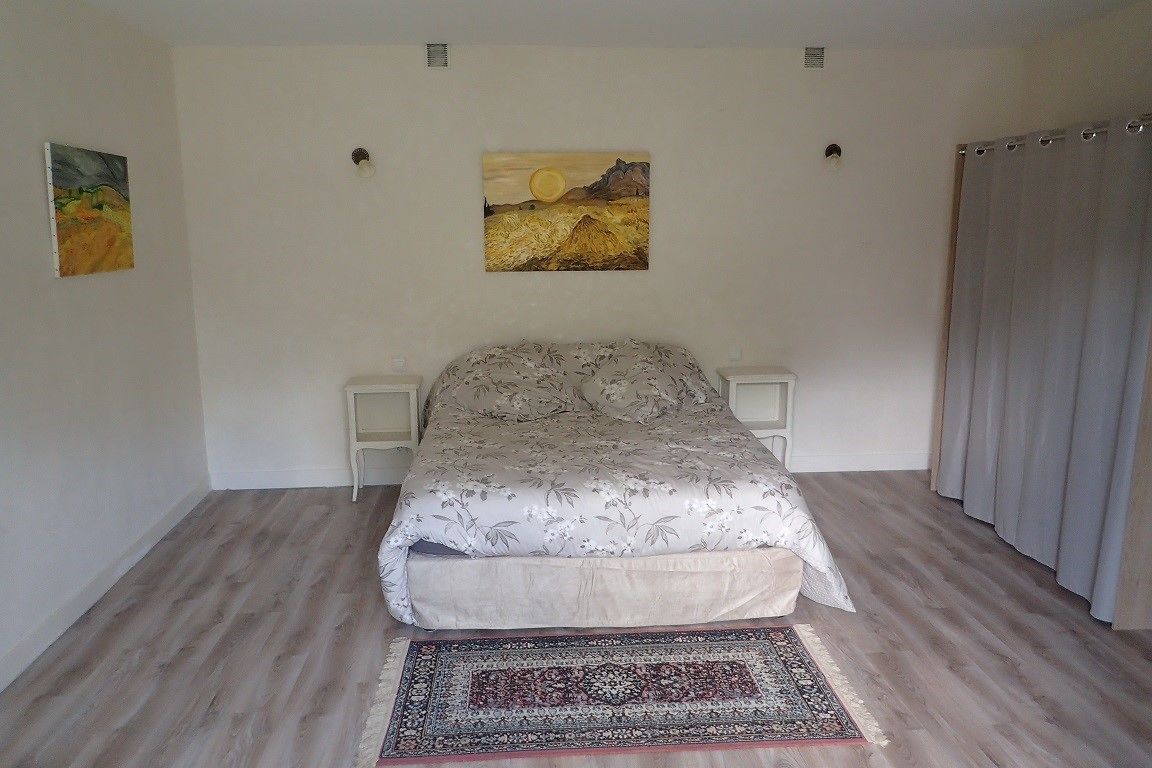 Un dormitorio con una cama, dos mesitas de noche, una alfombra y dos cuadros en la pared.