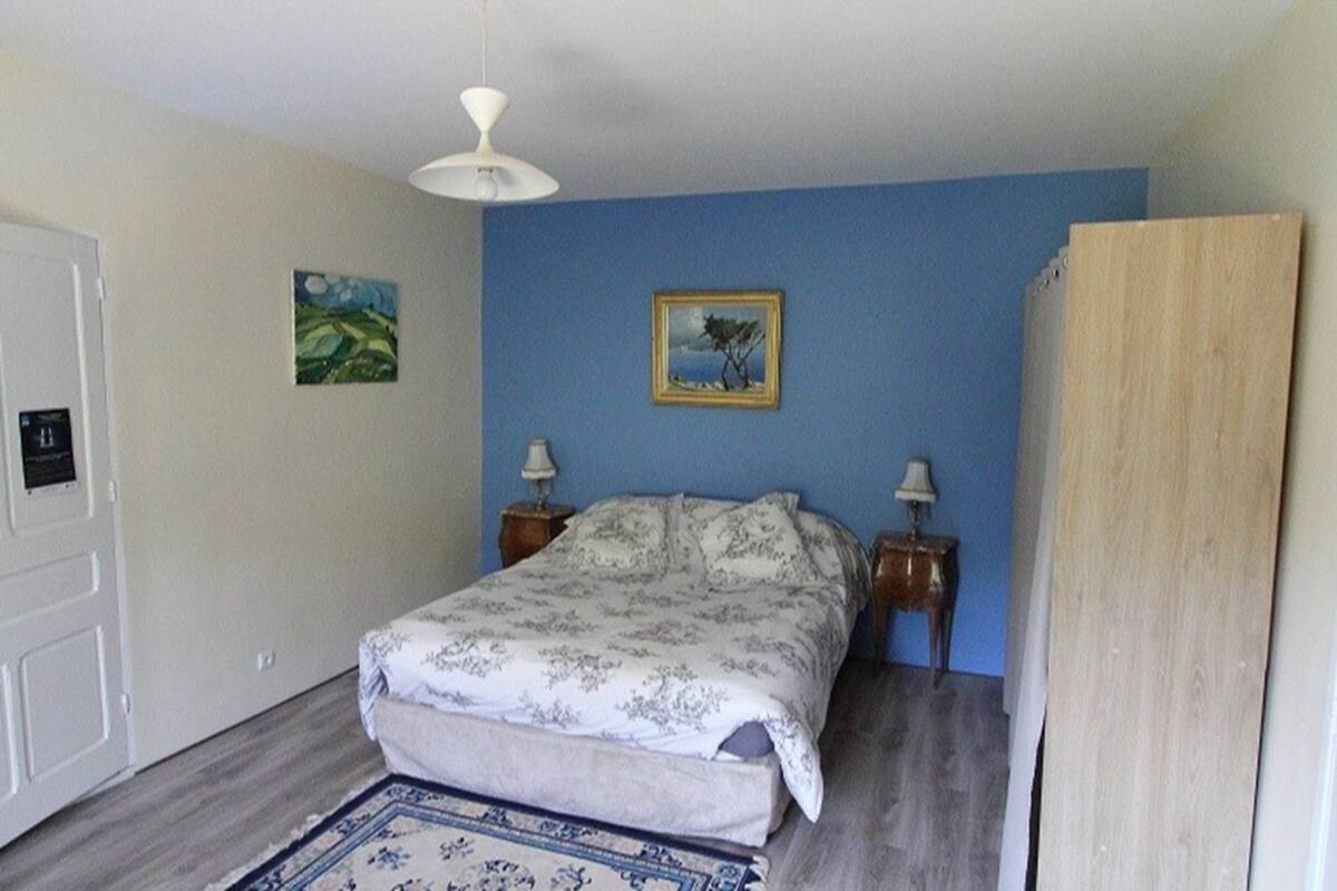 Un dormitorio con una cama, dos mesitas de noche, un ventilador de techo, un cuadro enmarcado y una puerta.