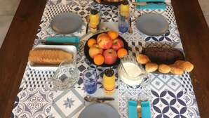 Uma longa mesa de jantar posta com diversos alimentos e bebidas, incluindo frutas, doces e acompanhamentos.