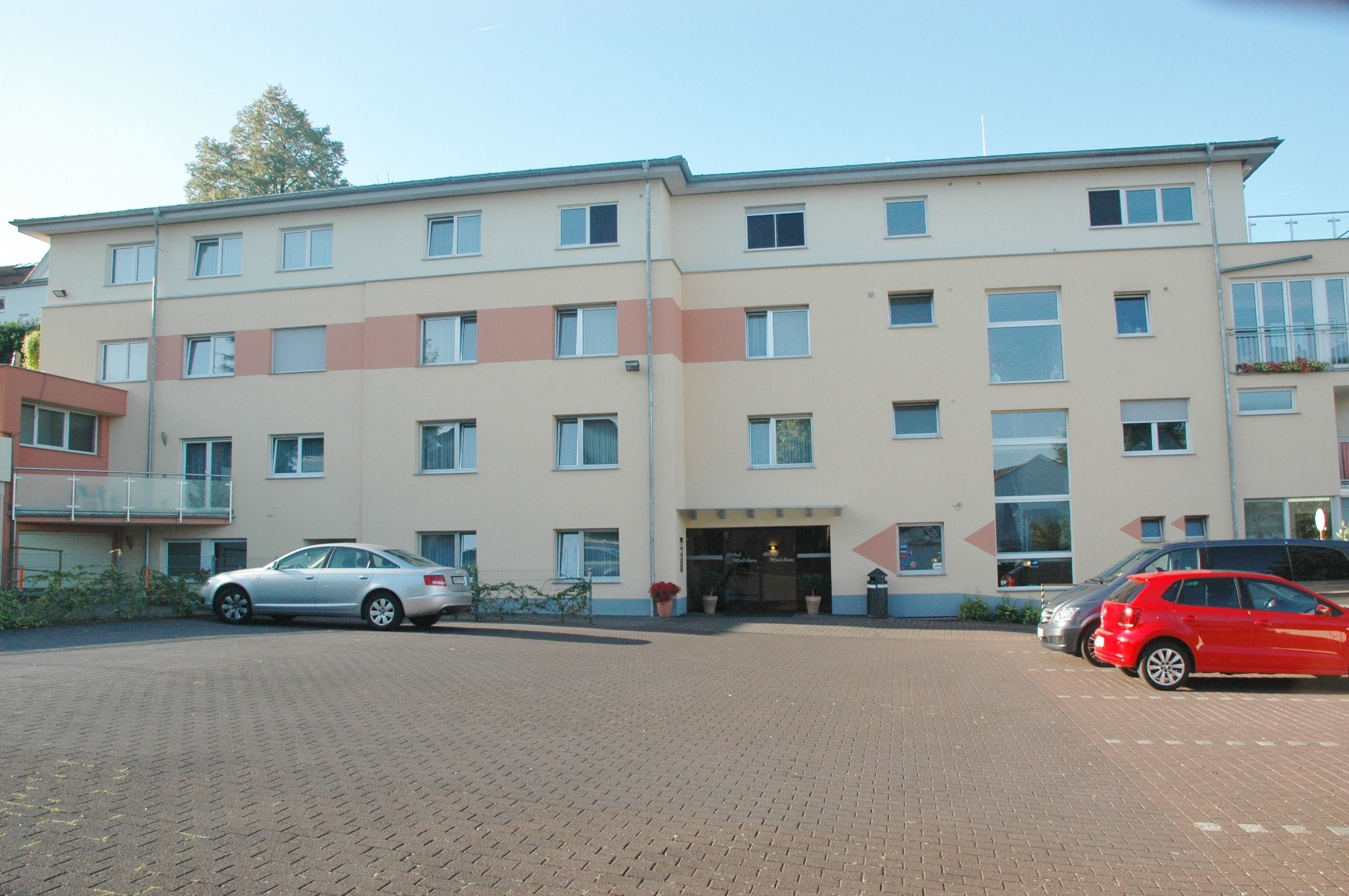 En bygning med flere etager, en flad facade, adskillige vinduer og en parkeringsplads med to biler.