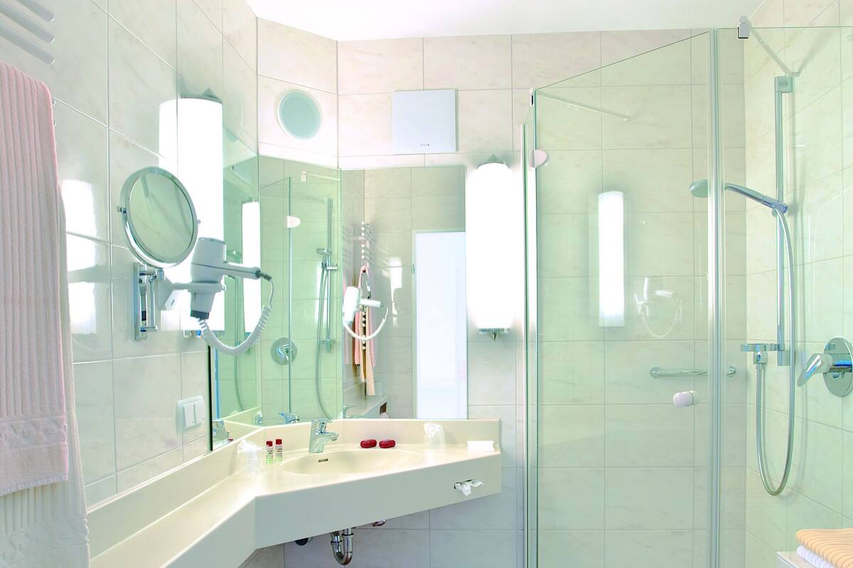 Un baño moderno con cabina de ducha de vidrio, lavamanos con espejo y toallero.