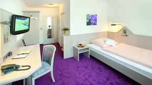 Habitación de hotel con cama, escritorio con silla, televisión, una mesita con un florero y un cuadro colgado en la pared.