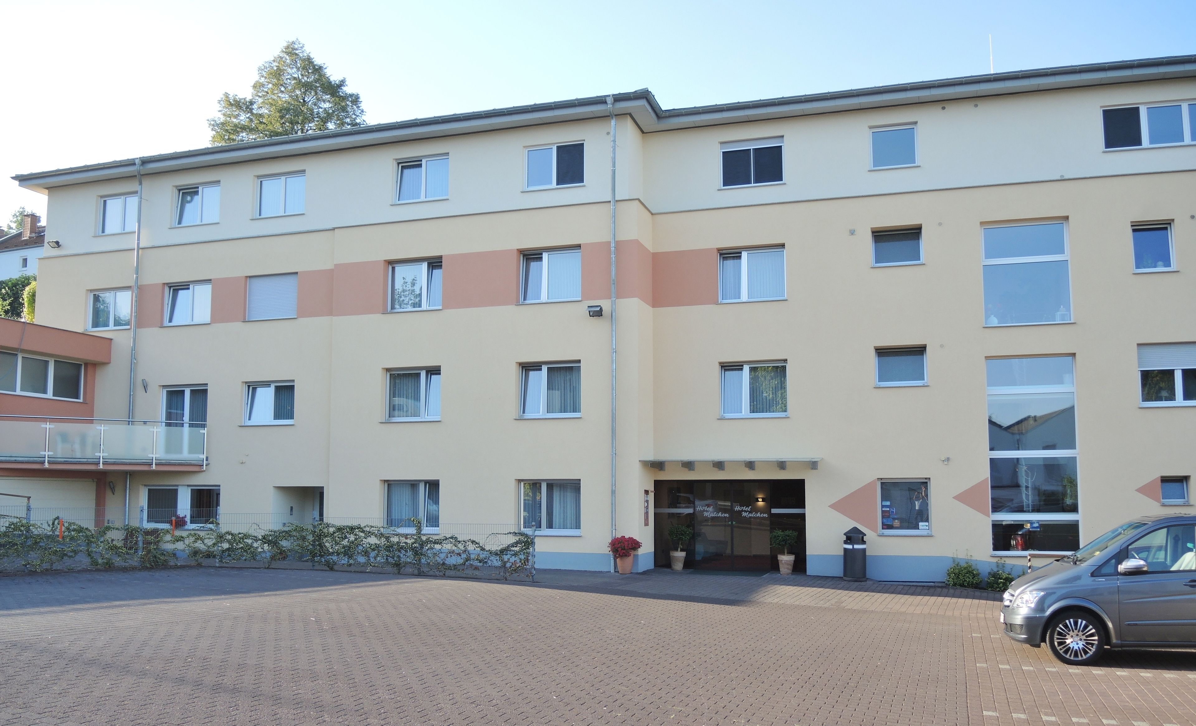 A multi-story hotel with a flat facade, multiple windows, and a paved entrance area.