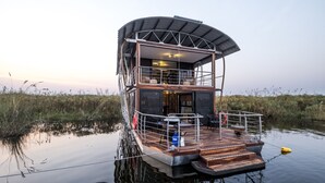 Ein schwimmendes Hausboot mit einer überdachten Deckterrasse, einem Essbereich und einer kleinen Sitzgelegenheit im Freien.