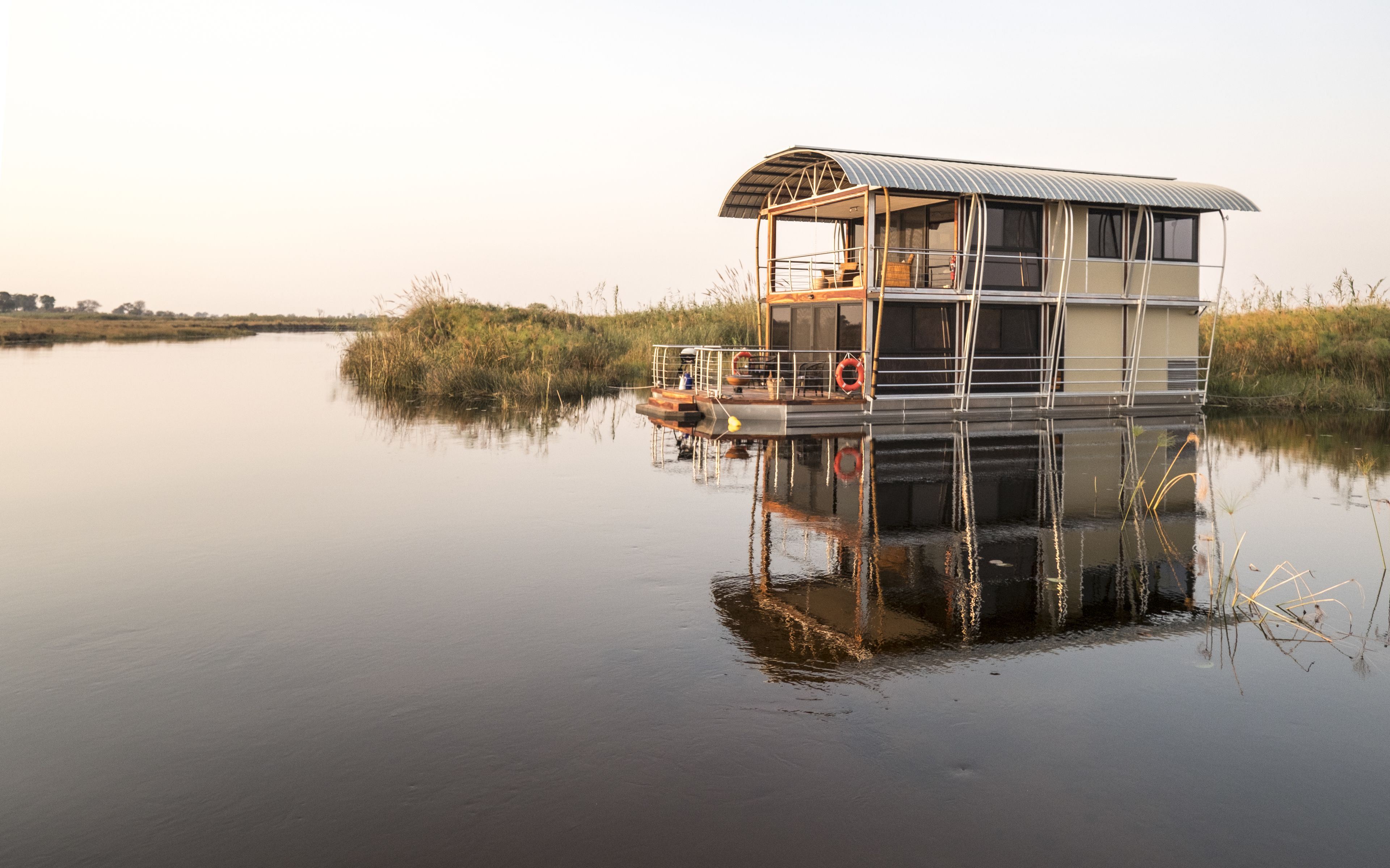 Ein Hausboot mit überdachter Terrasse, einer kleinen Sitzgelegenheit im Freien und einem Rettungsring.