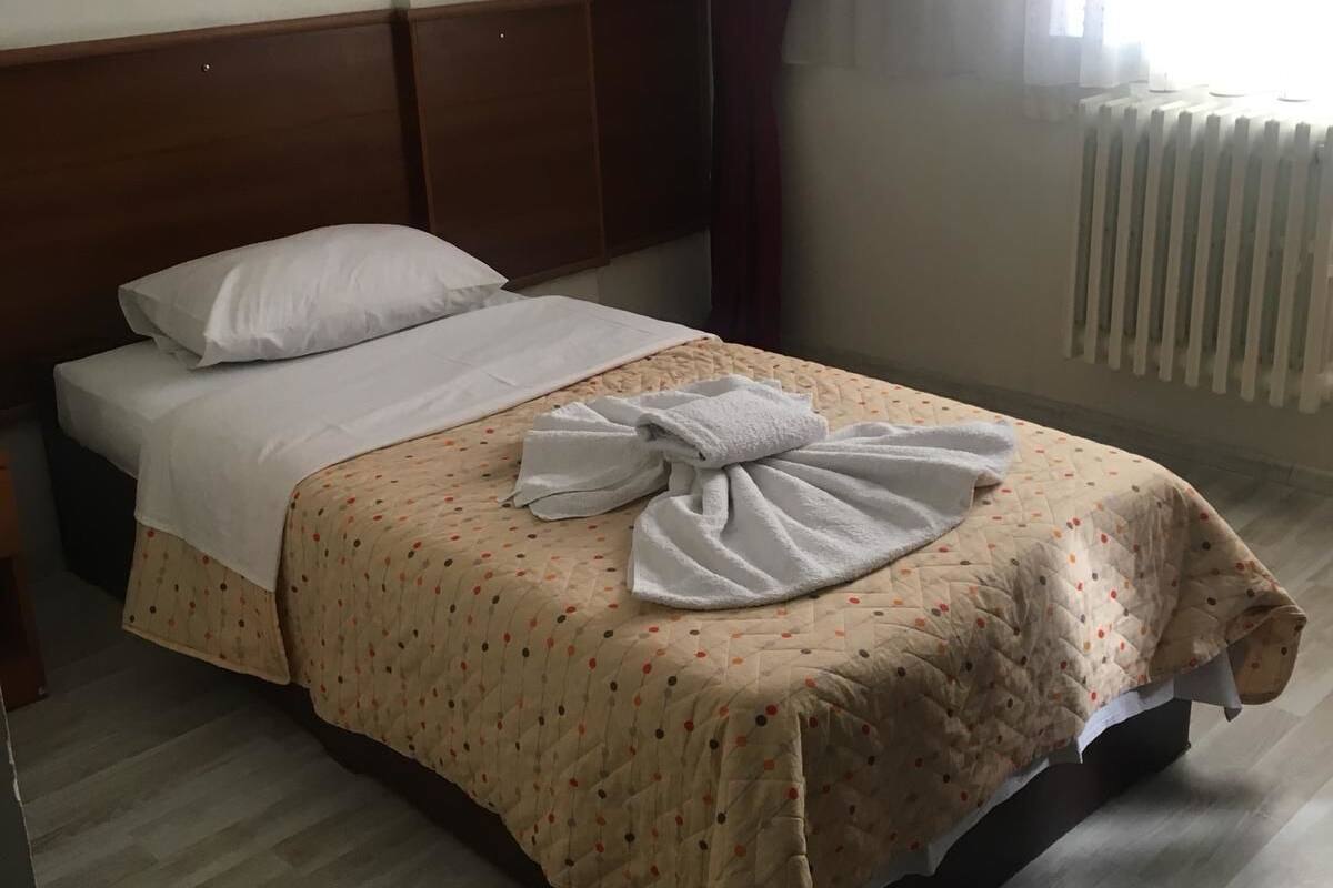 Ein aufgeräumtes Bett mit einer gesteppten Decke, einem Holzkopfende und einem Fenster mit Vorhängen.