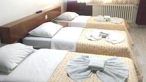 Ett hotellrum med tre enkelsängar, var och en med en vit kudde och ett vitt täcke. Sängarna har mönstrade sängöverdrag. Den vänstra sängen har en träfärgad sänggavel, och en element syns i bakgrunden.