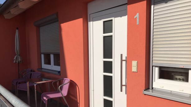 A small outdoor seating area with a table and chairs, a door with a window, and a sliding glass door. - Gästehaus Durst (Rust)
