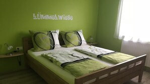 A bed with green bedding, a bedside table with a lamp, and a wall with a sign. - Gästehaus Durst (Rust)