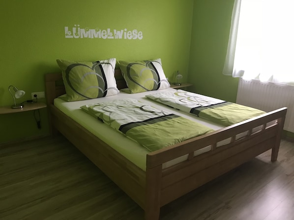 A bed with green bedding, a bedside table with a lamp, and a wall with a sign. - Gästehaus Durst (Rust)