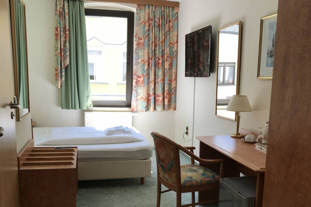 Een hotelkamer met een bed, een bureau, een stoel, een televisie en een raam met gordijnen.