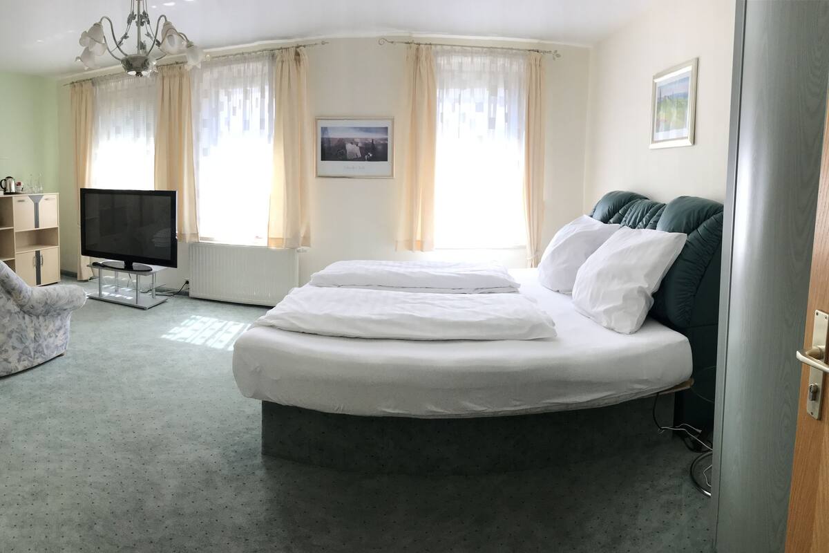 Een slaapkamer met een bed, een televisie, een stoel en een raam met gordijnen.
