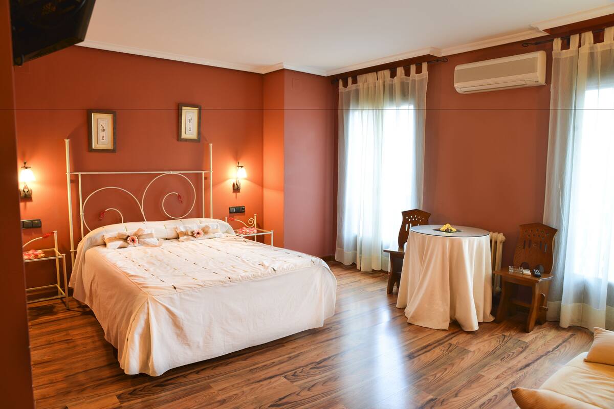 A bedroom with a large bed, bedside tables, a round table, and a chair.