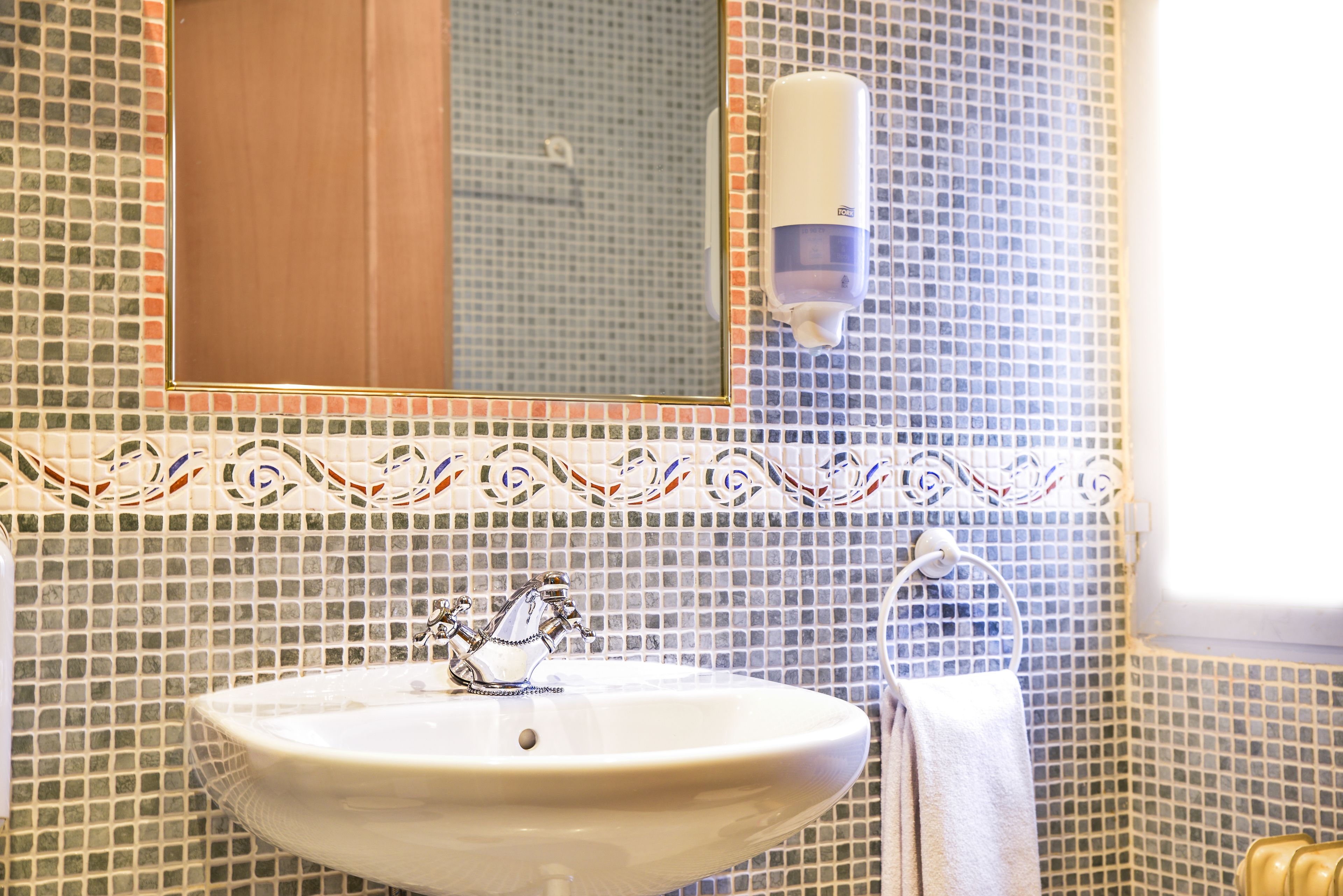 A bathroom with a sink, mirror, and soap dispenser.