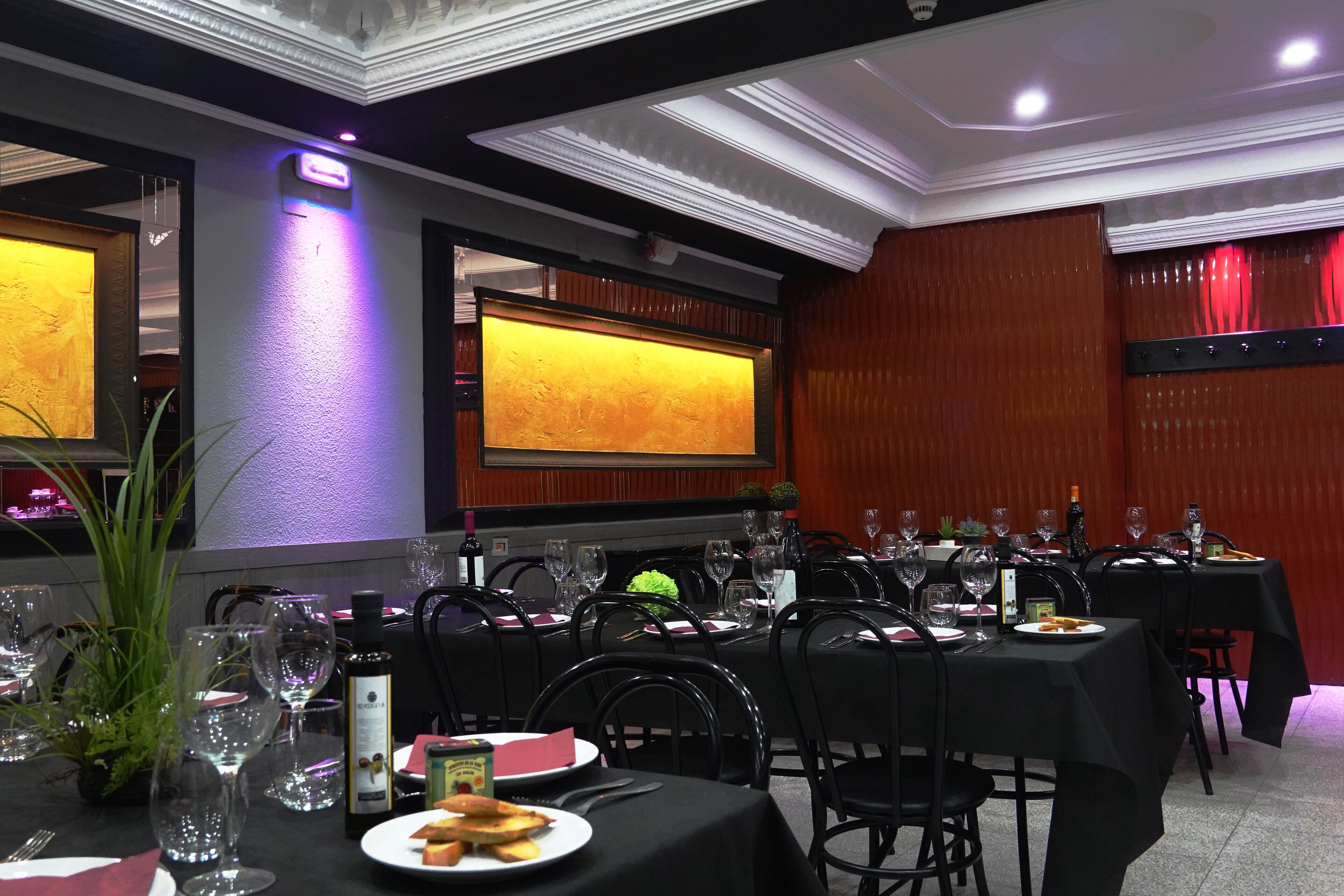 Un restaurante con mesas dispuestas para comer, con un interior moderno que incluye una pared iluminada y luces de techo.