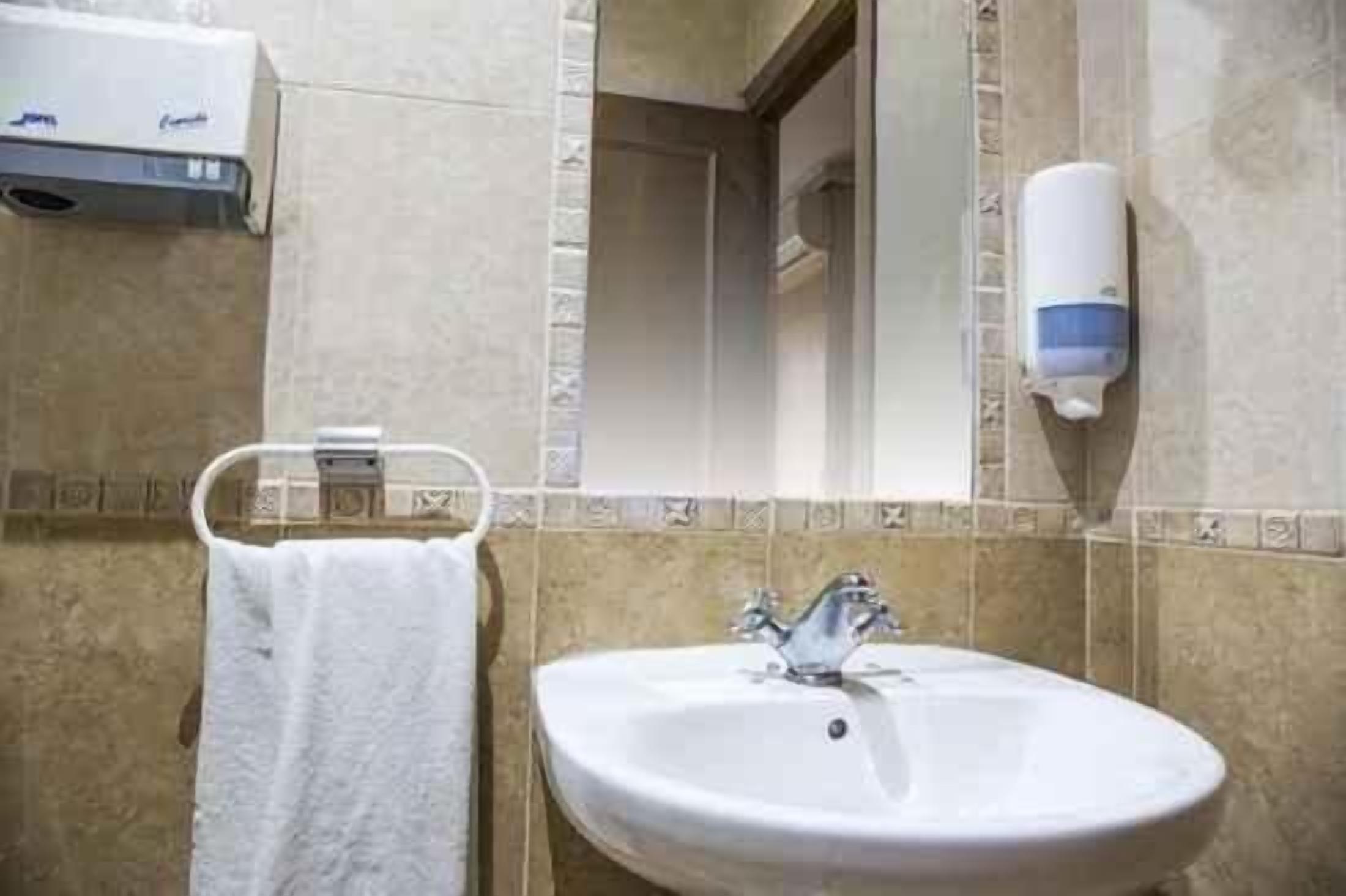 A bathroom with a white sink, a towel rack with a white towel, a hand soap dispenser, and a mirror.