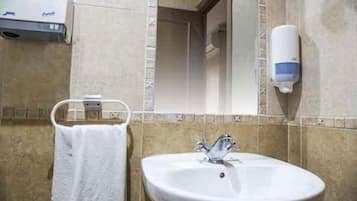 Un baño con un lavabo blanco, un toallero con una toalla blanca, un dispensador de jabón para manos y un espejo.