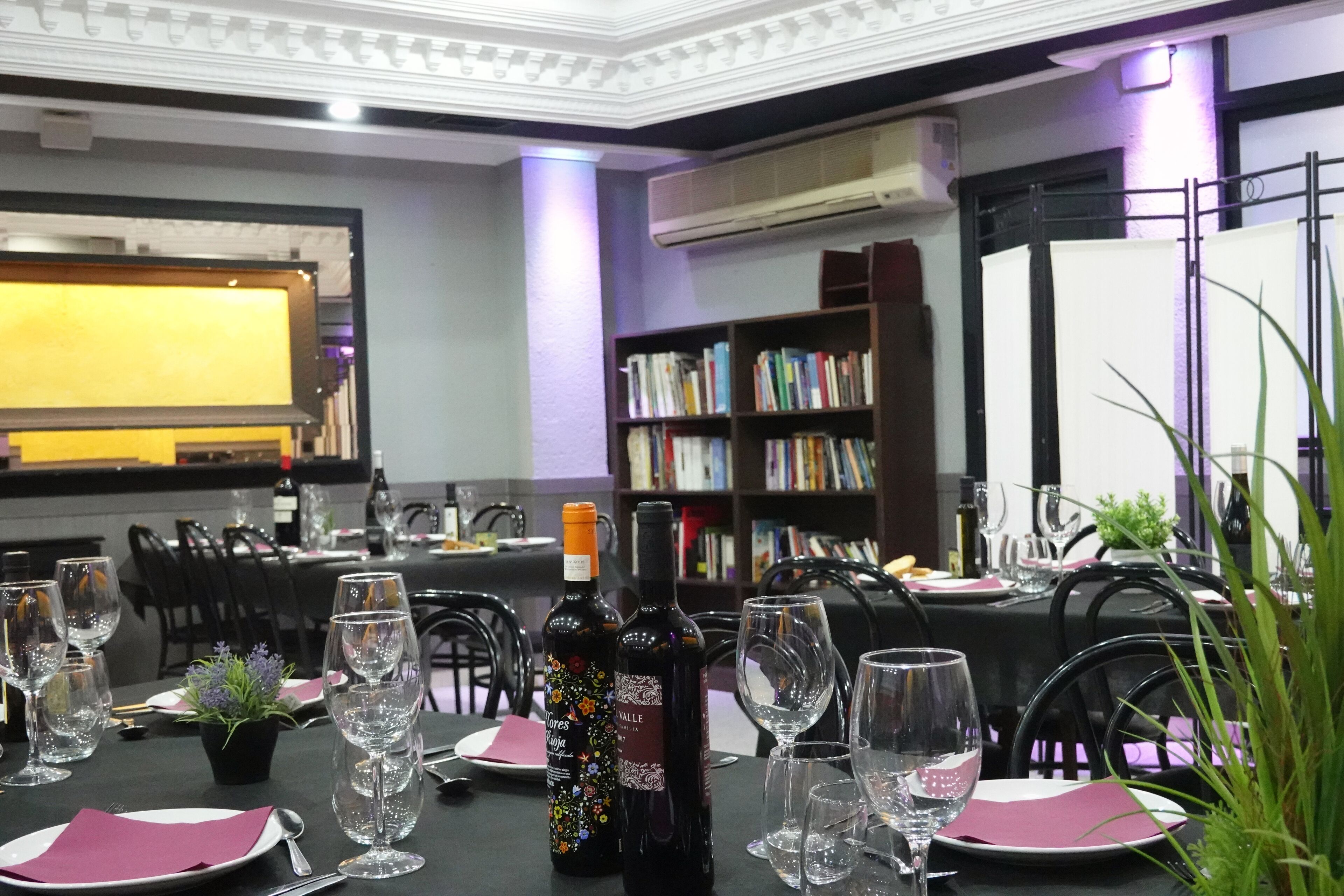 Un comedor con mesas dispuestas para una comida, botellas de vino y una estantería al fondo.
