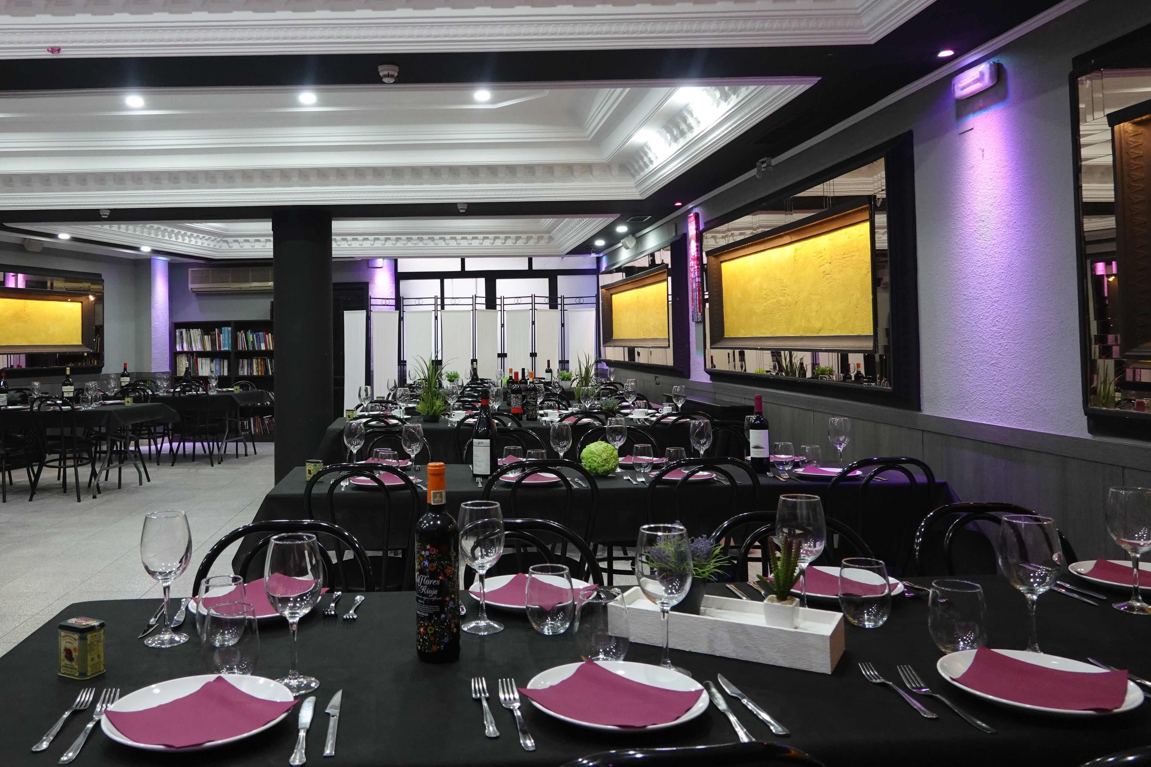 A banquet hall with tables set for dining, a stage with a large screen, and a bar area with bottles and glasses.