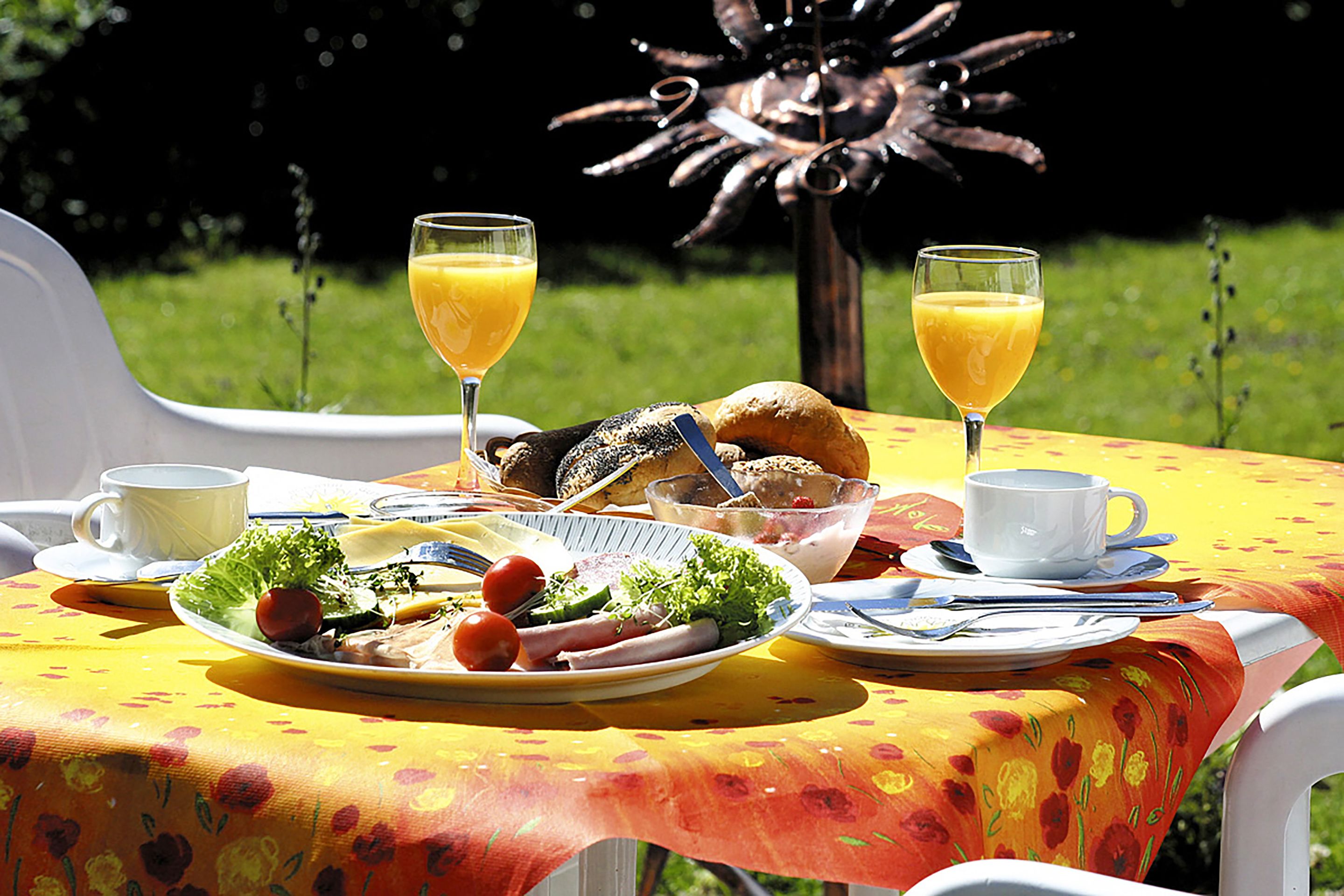 Ein Tisch, gedeckt mit Frühstücksangeboten, darunter Teller mit Speisen, Gläser Orangensaft und eine Tasse.