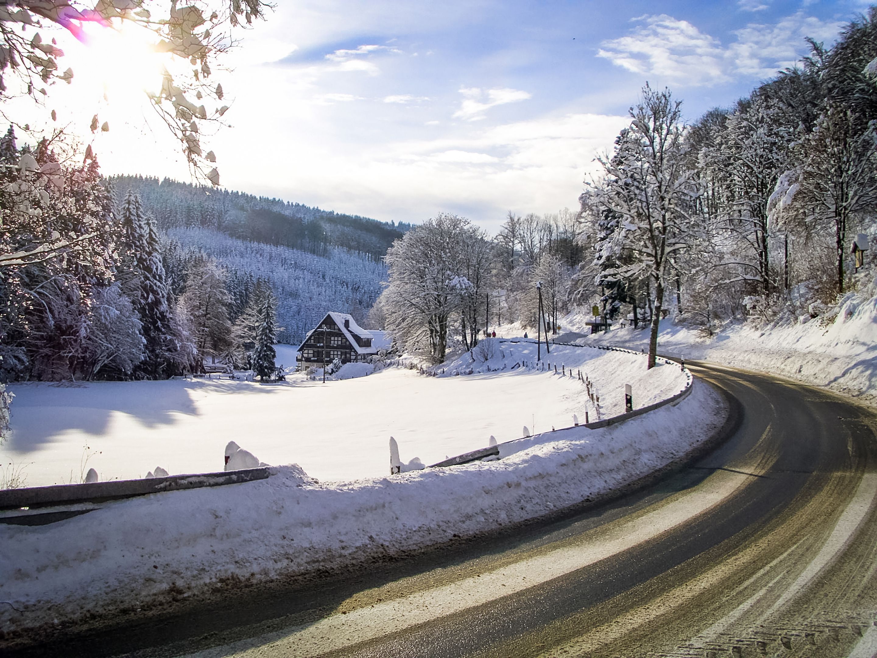Schneebedeckte Landschaft mit einer kurvenreichen Straße, einer Holzhütte und schneebedeckten Bäumen.