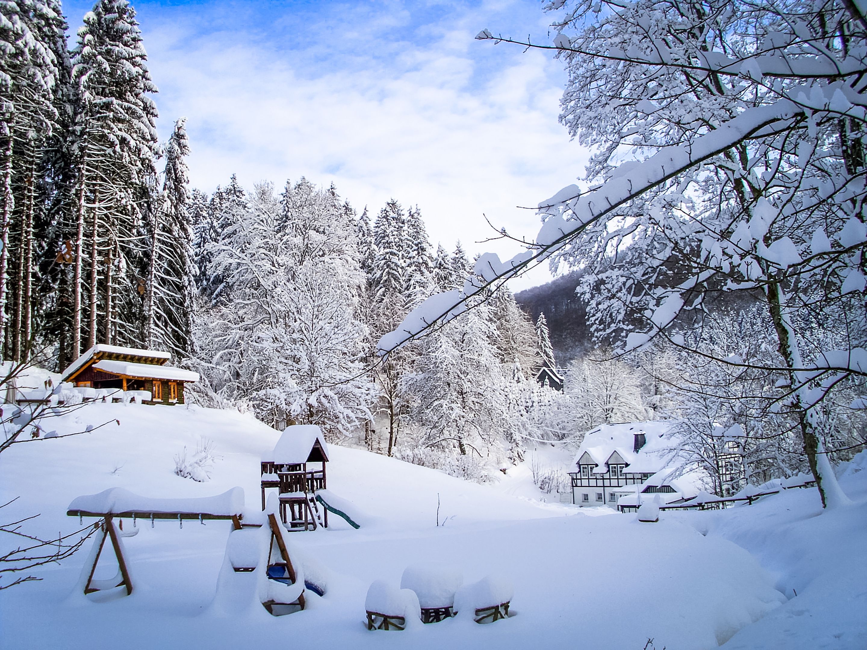 Eine verschneite Holzhütte mit einer Holzterrasse und einer kleinen Spielanlage.