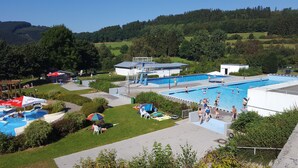 Zona de piscina con varias piscinas, una plataforma de salto y vegetación circundante.
