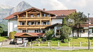A multi-story building with a wooden balcony, a sign reading "Landhaus MARZ," and a mountain backdrop. - Landhaus Marga (Fischen im Allgaeu)