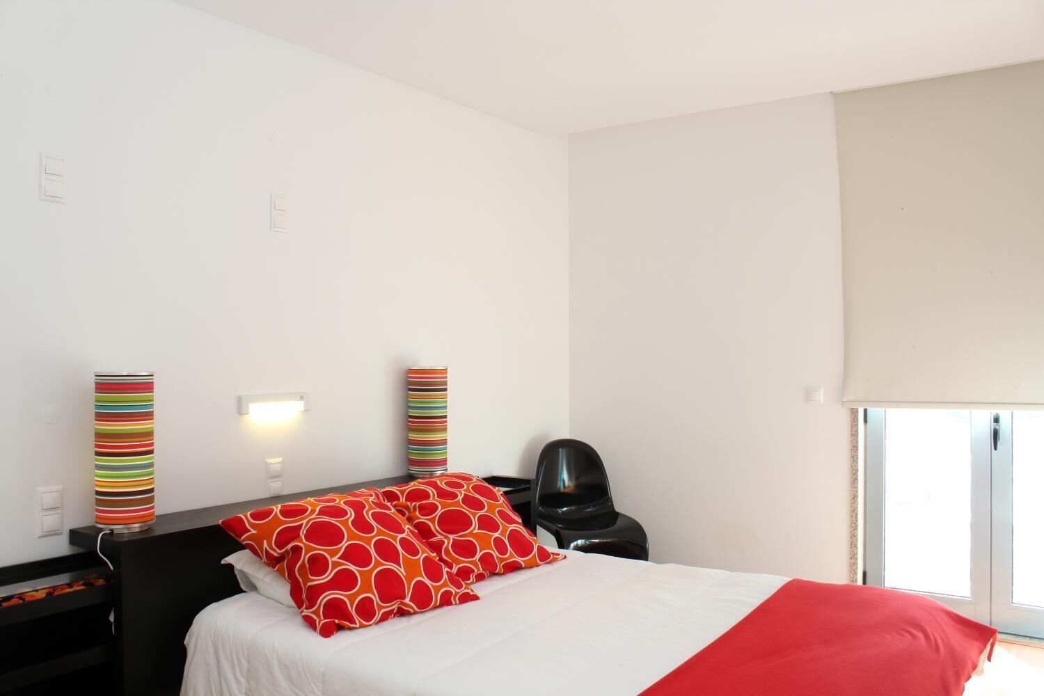 A hotel room with a bed, a chair, a bedside table, a lamp, and a window.