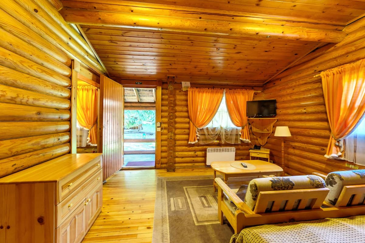 A log cabin room with a wooden interior, a television, a sofa, a table, and a window with curtains.