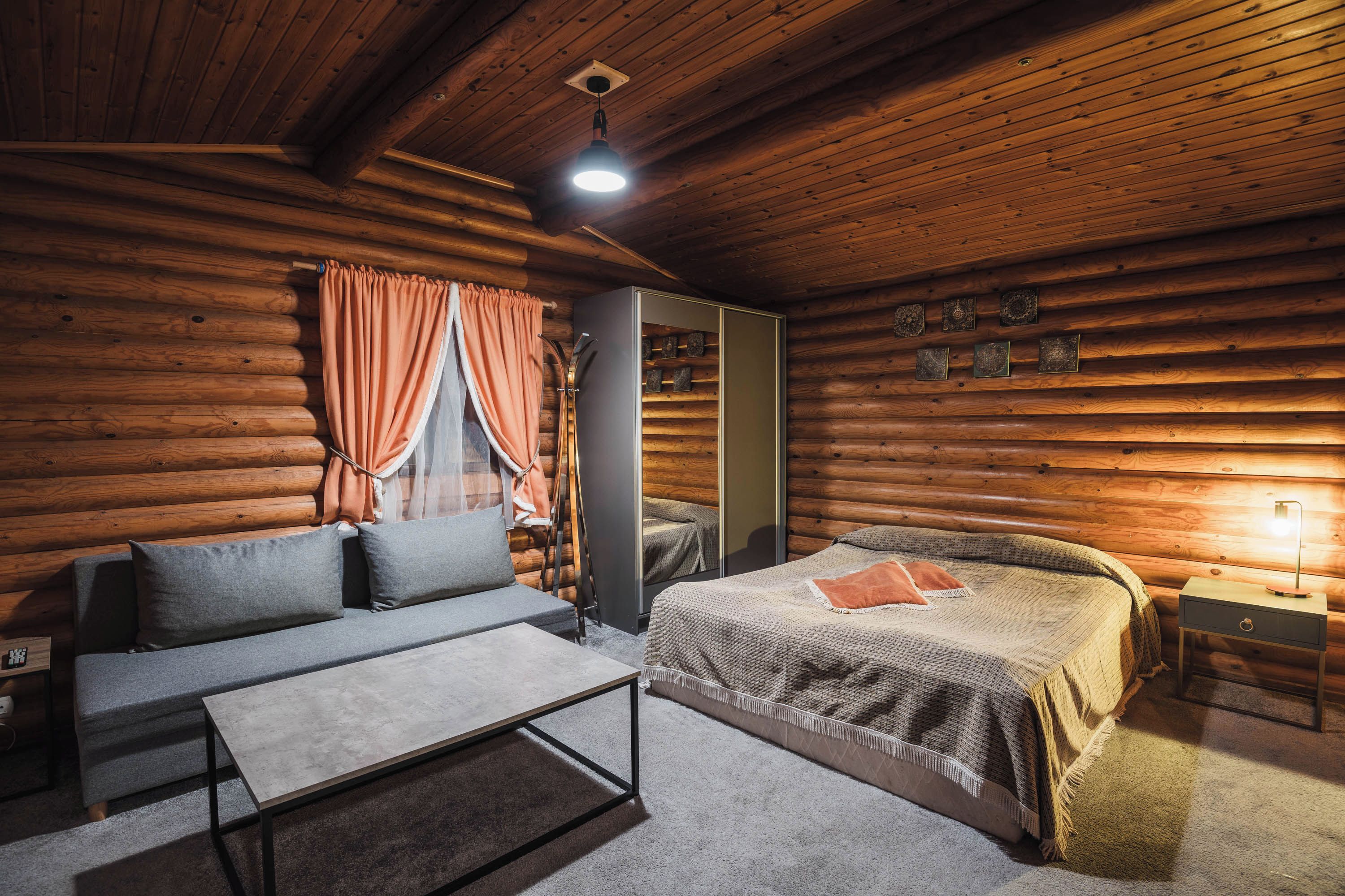 A log cabin bedroom with a bed, a sofa, a table, and a nightstand.