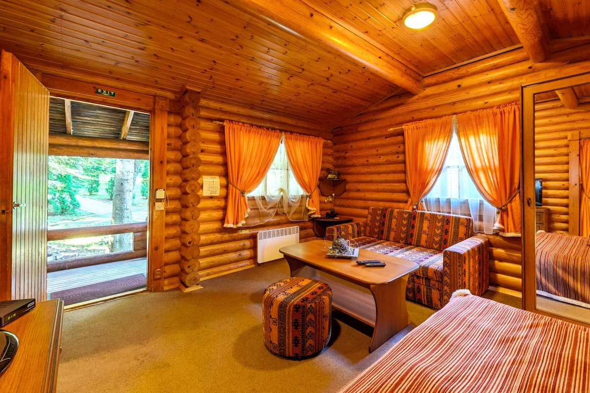 A log cabin interior with a wooden dining table, benches, and a sofa.
