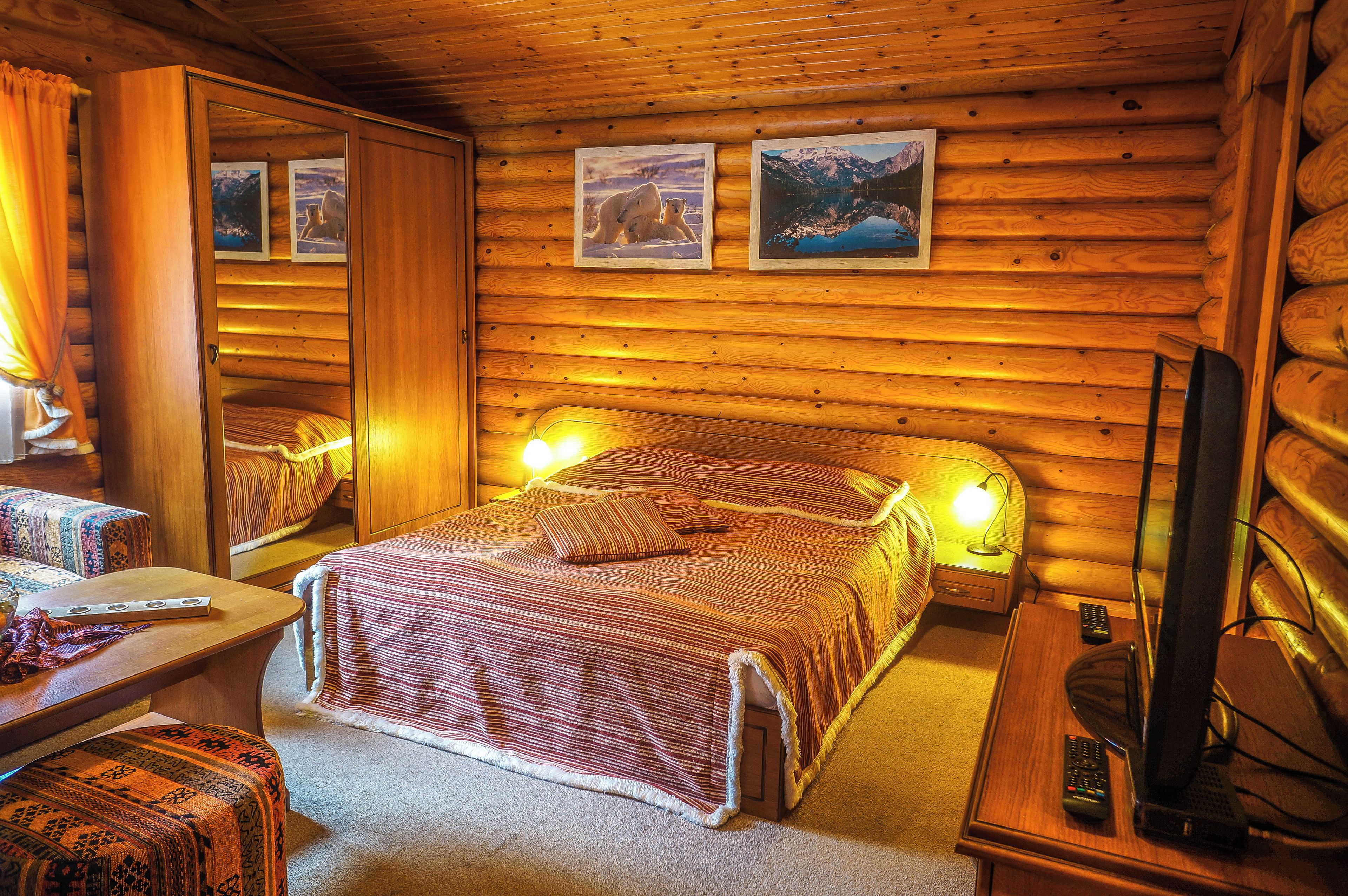 Ein gemütliches Blockhaus-Zimmer mit einem Bett, einem Sessel, einem Tisch und einem Fernseher.