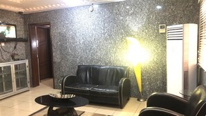 Habitació amb un sofà de pell negra, una taula rodona petita, una làmpada de peu i un moble amb televisió.