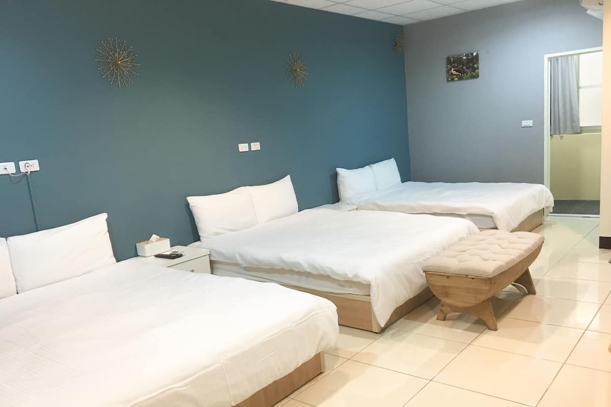A hotel room with three beds, a wooden bench, and a blue wall with decorative star-like patterns.