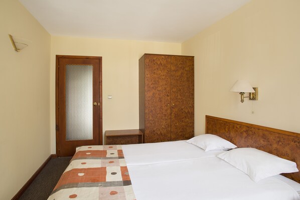 Une chambre d’hôtel avec un lit, une armoire en bois, une petite table et une lampe fixée au mur.
