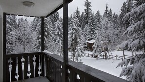 Un balcón de madera con vistas a árboles cubiertos de nieve y una cabaña al fondo.