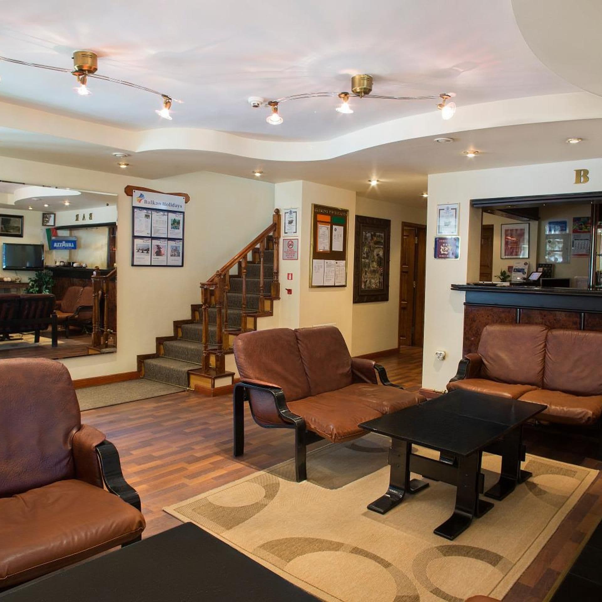 A lobby with leather sofas, a staircase, a reception desk, and a wall with holiday information.