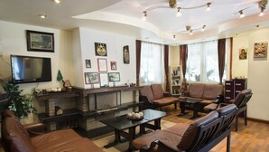 A living room with leather sofas, a fireplace, a flat-screen TV, and a bookshelf. - Victoria Borovets (Boboshevo)