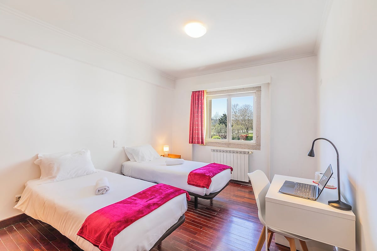 Une chambre d’hôtel avec deux lits, un bureau avec un ordinateur portable, une fenêtre donnant sur un paysage agréable et un radiateur.