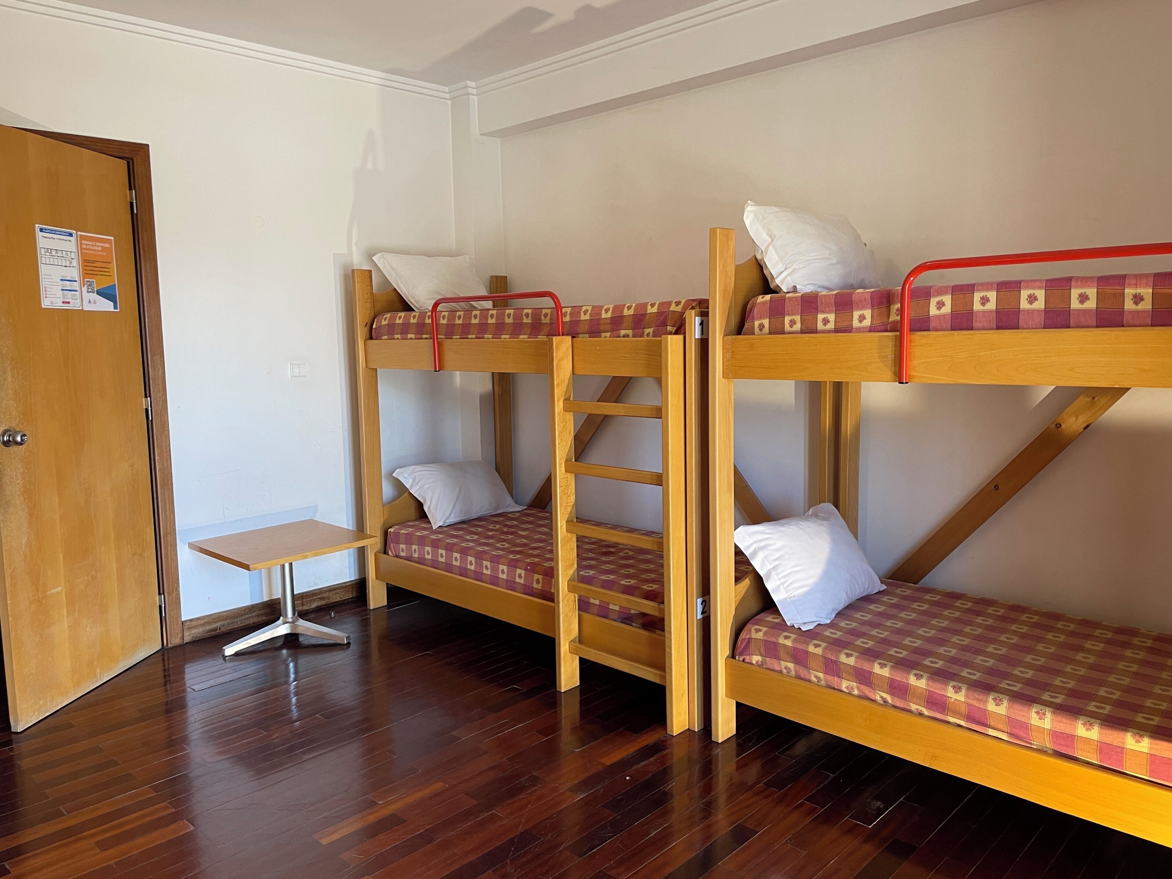 Una habitación con tres literas, una puerta de madera y una mesita pequeña.