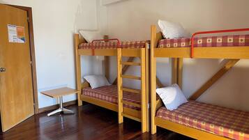 Una habitación con tres literas, una puerta de madera y una mesita pequeña.