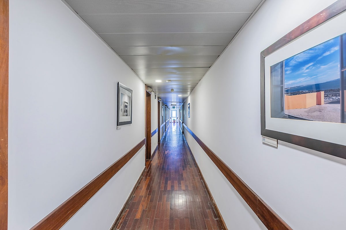 Un couloir avec des tableaux encadrés accrochés aux murs, un plancher en bois et une grande fenêtre sur le côté droit.