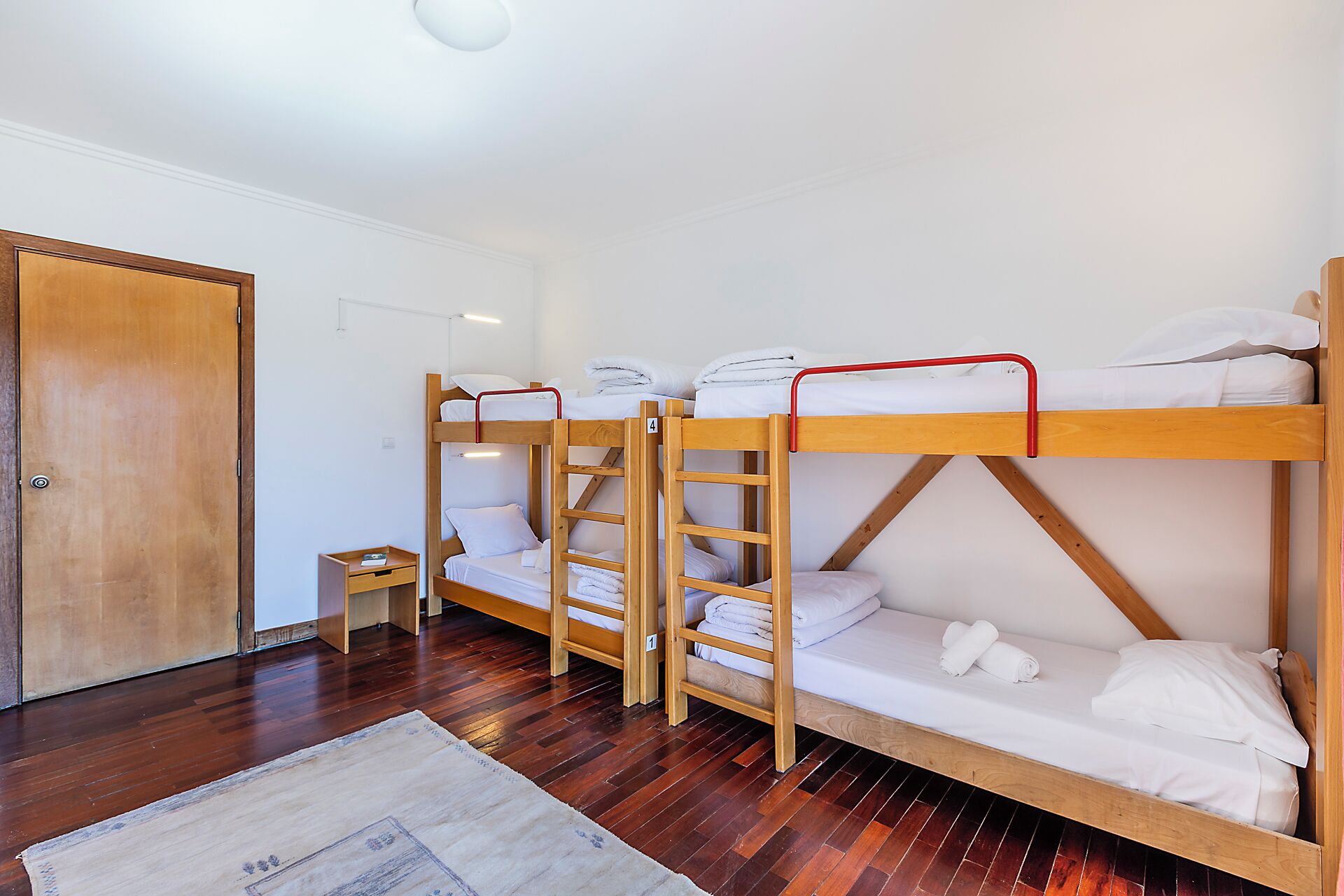 A bunk bed room with wooden frames, white bedding, and a small wooden nightstand.