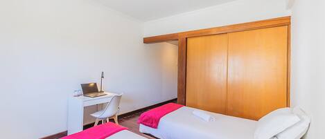 A hotel room with two beds, a desk, and a wardrobe.