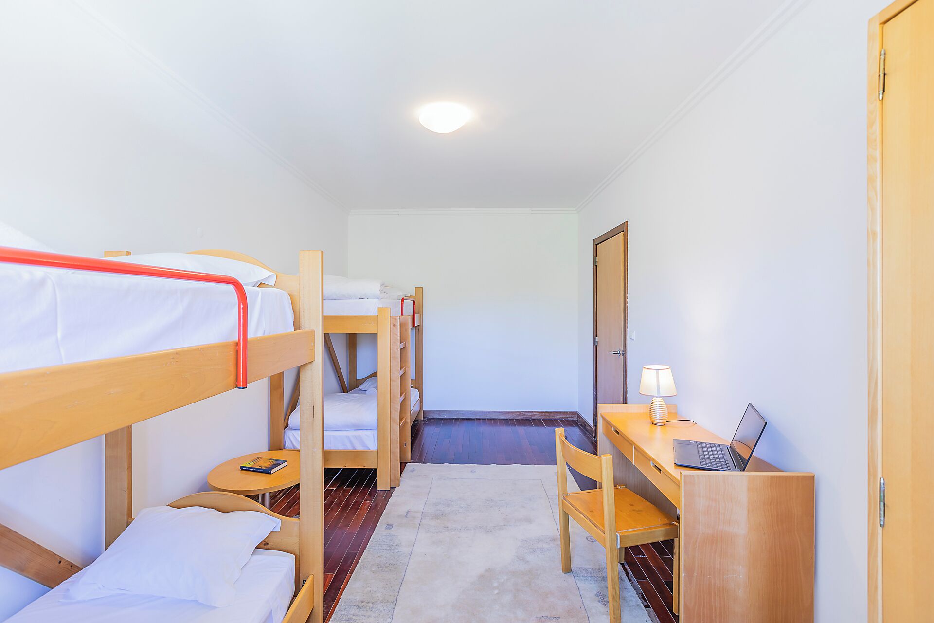 A room with bunk beds, a desk with a laptop, a lamp, and a door.