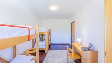 A room with bunk beds, a desk with a laptop, a lamp, and a door.