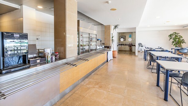 Eine moderne Hotelhalle mit Selbstbedienungs-Frühstücksbuffet, einer Sitzecke und einer großen Pflanze.