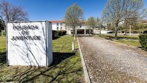 Ein Schild mit der Aufschrift 'POUSADA DE JUVENTUDE' vor einem Gebäude mit Kiesweg und Bäumen.