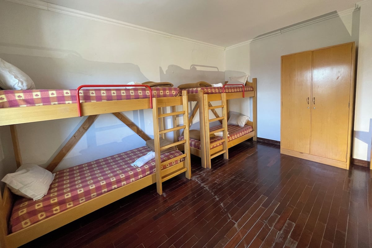 Une chambre avec un lit superposé, un plancher en bois, une armoire et un luminaire au plafond.